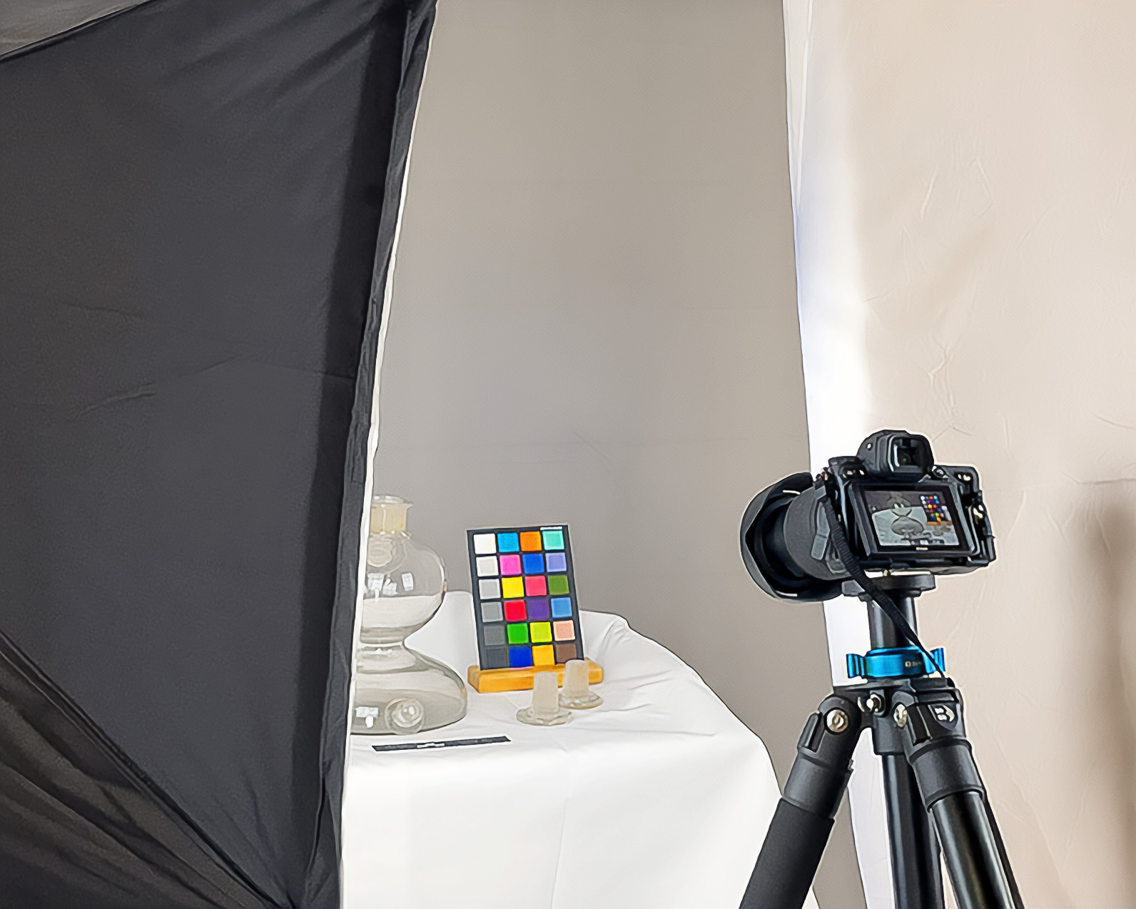 Photo documentation in the museum: a glass oil-lamp base on white cloth beside a colour chart, with a camera on a tripod at the right